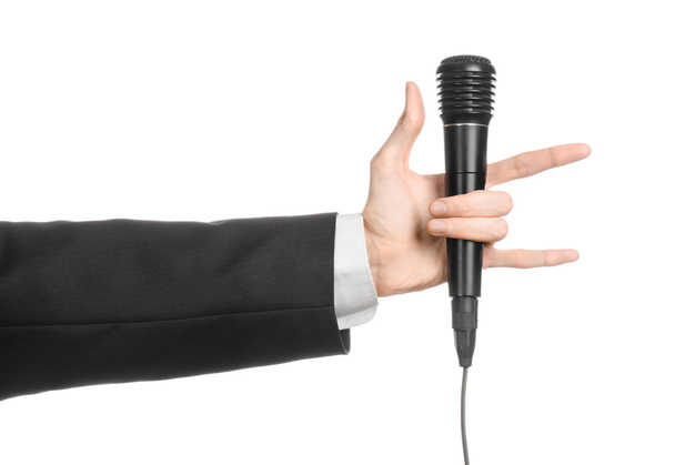 Business and speech topic: Man in black suit holding a black microphone isolated on white background in studio - Valokuva, kuva