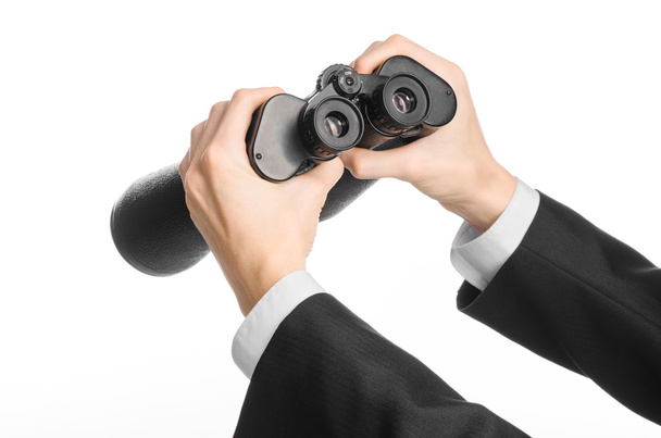 Business and search topic: Man in black suit holding a black binoculars in hand on white isolated background in studio - Foto, Bild