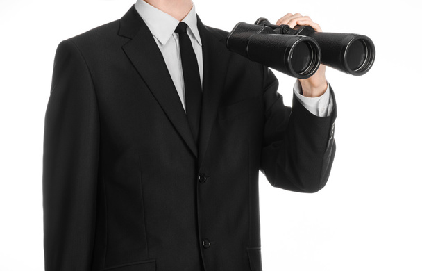 Business and search topic: Man in black suit holding a black binoculars in hand on white isolated background in studio - Foto, Imagen