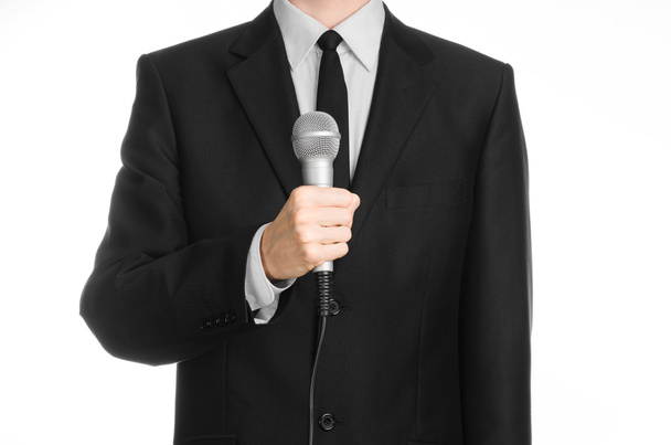 Business and speech topic: Man in black suit holding a gray microphone on an isolated white background in studio - Фото, зображення