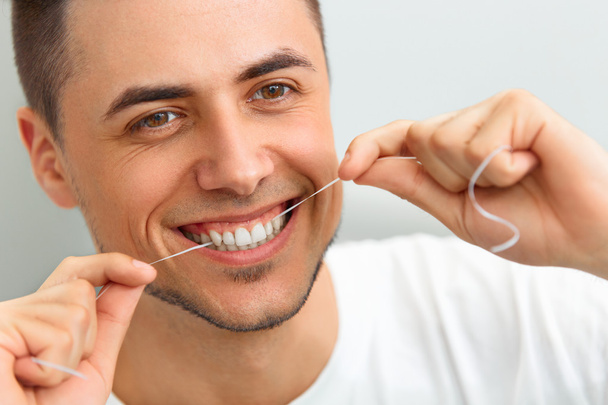 Closeup of young man flossing his teeth. Cleaning teeth with den - 写真・画像