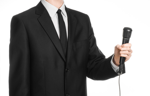 Business and speech topic: Man in black suit holding a black microphone isolated on white background in studio - Fotoğraf, Görsel