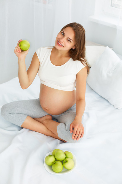 Pregnant Young Woman holding Apple while sitting on the Bed. Hea - 写真・画像