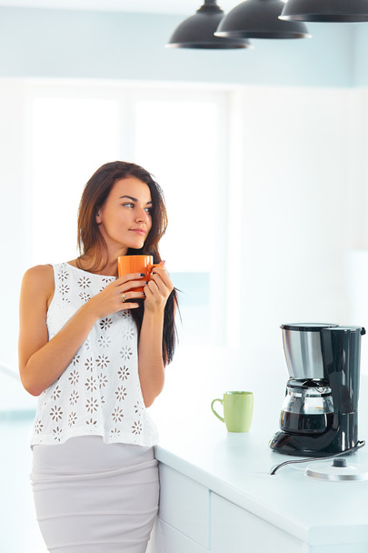 Woman holding a cup of coffee in her kitchen - Foto, Imagen