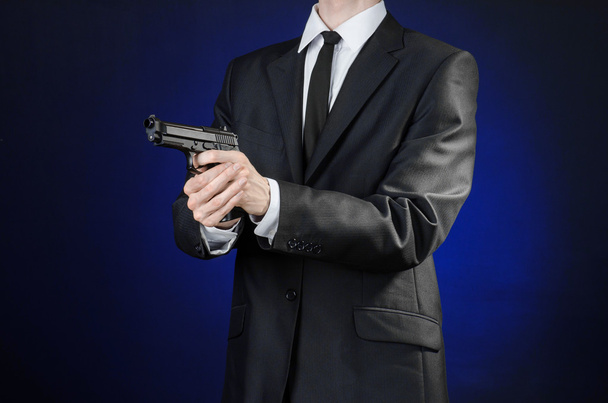 Firearms and security topic: a man in a black suit holding a gun on a dark blue background in studio isolated - Foto, Imagem