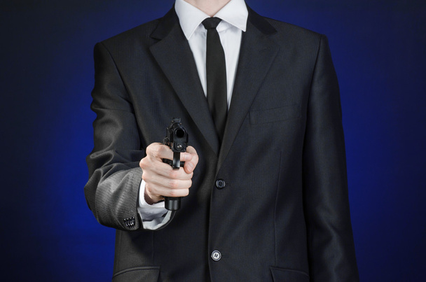 Firearms and security topic: a man in a black suit holding a gun on a dark blue background in studio isolated - Foto, Bild
