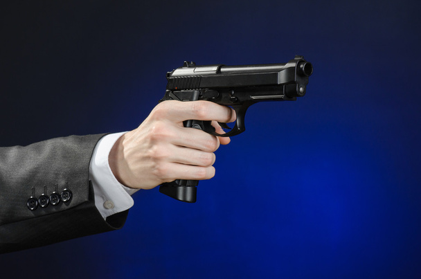 Firearms and security topic: a man in a black suit holding a gun on a dark blue background in studio isolated - Foto, imagen