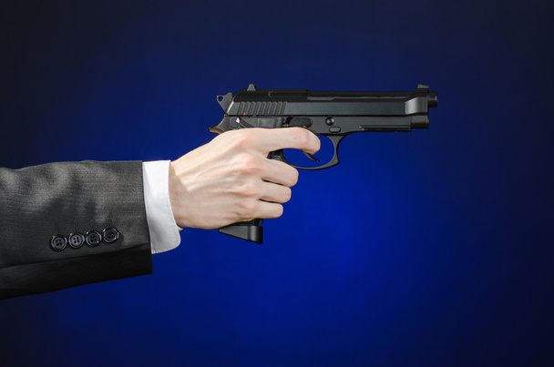 Firearms and security topic: a man in a black suit holding a gun on a dark blue background in studio isolated - Valokuva, kuva
