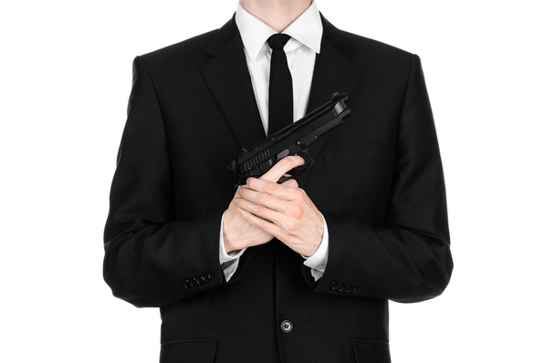 Firearms and security topic: a man in a black suit holding a gun on an isolated white background in studio - Valokuva, kuva
