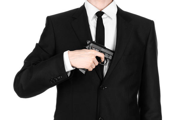 Firearms and security topic: a man in a black suit holding a gun on an isolated white background in studio - Photo, Image