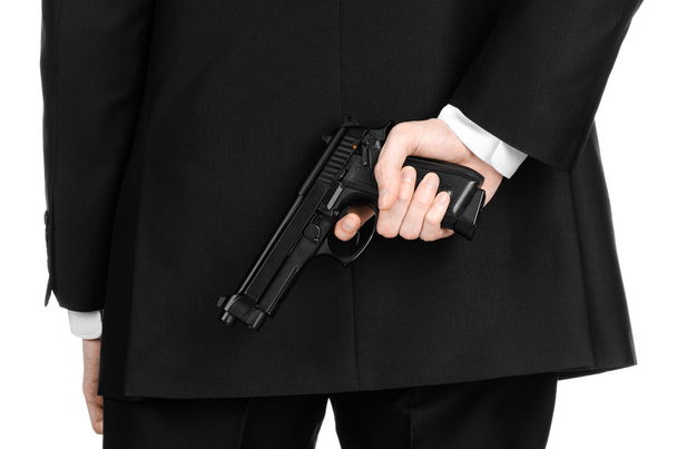 Firearms and security topic: a man in a black suit holding a gun on an isolated white background in studio - Фото, изображение