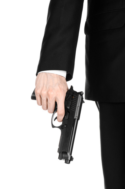 Firearms and security topic: a man in a black suit holding a gun on an isolated white background in studio - Zdjęcie, obraz