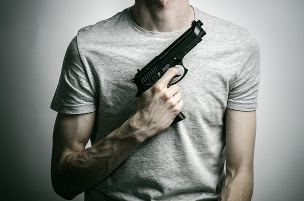 Horror and firearms topic: suicide with a gun on a gray background in the studio - Foto, imagen