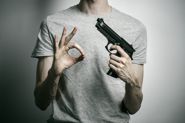 Horror and firearms topic: suicide with a gun on a gray background in the studio - Foto, Imagen