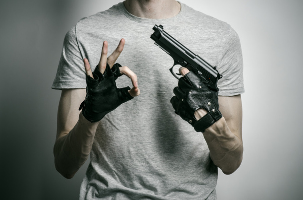 Horror and firearms topic: the killer with a gun in his hand in black gloves on a gray background in the studio - Fotó, kép