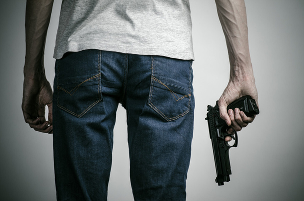 Horror and firearms topic: crazed killer with a gun on a gray background in the studio - Fotó, kép