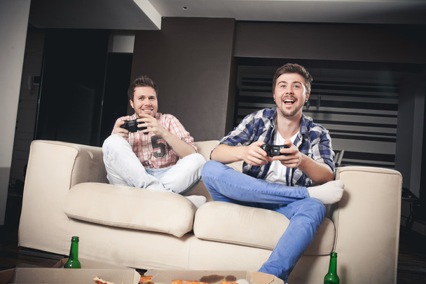 Two young men playing video games while sitting on sofa - Foto, Imagem