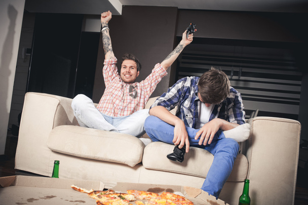 Two young men playing video games while sitting on sofa - Foto, Imagen