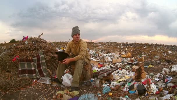férfi hajléktalan koldus ül a hulladéklerakó egy kalap kéri pénzt élelmiszer-hulladék - Felvétel, videó