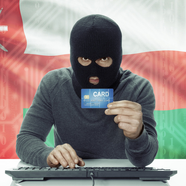 Dark-skinned hacker with flag on background holding credit card in hand - Oman - Foto, imagen