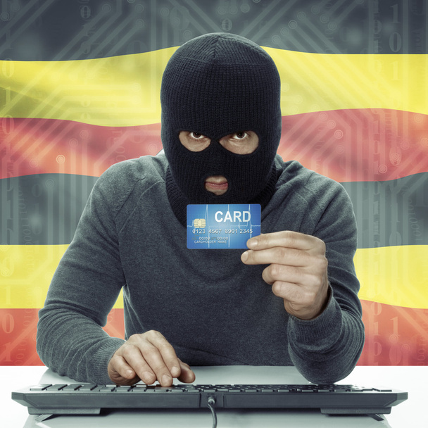 Dark-skinned hacker with flag on background holding credit card in hand - Uganda - Foto, imagen