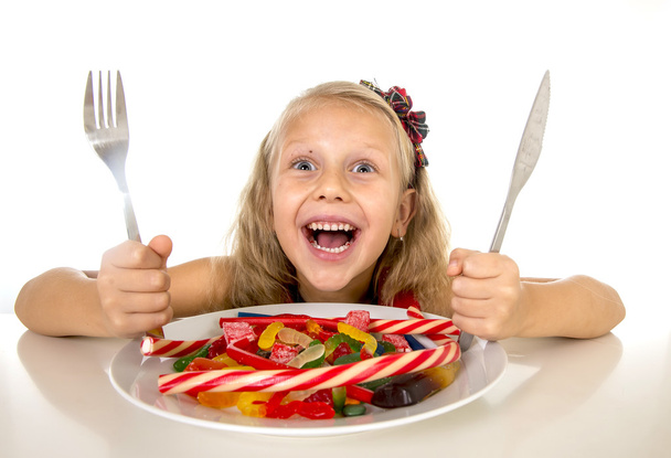 pretty happy Caucasian female child eating dish full of candy in sweet sugar abuse dangerous diet - Photo, Image