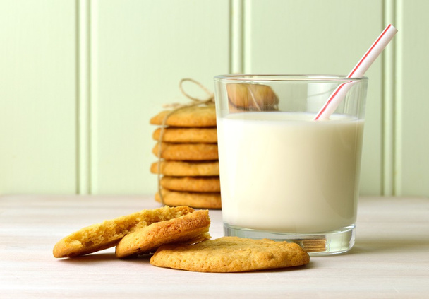 Verfrissende glas melk met een drinken stro, en een heerlijke snack van zelfgemaakte peanut butter cookies. Met een gebonden stck van cookies op de achtergrond. - Foto, afbeelding