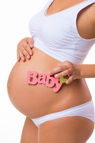 Pink label "Baby" a kezében terhes nő. Az újszülött lánya. Terhes hasa közelről, fehér alapon. - Fotó, kép