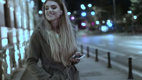 Mujer escuchando música en el teléfono celular caminando por la noche
 - Imágenes, Vídeo