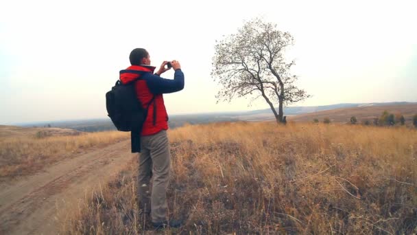 man hiker traveler with a backpack in the autumn is on the way to nature is a solitary tree travel - Imágenes, Vídeo