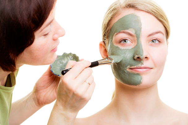 Cosmetician applying clay facial mask at woman face. - 写真・画像