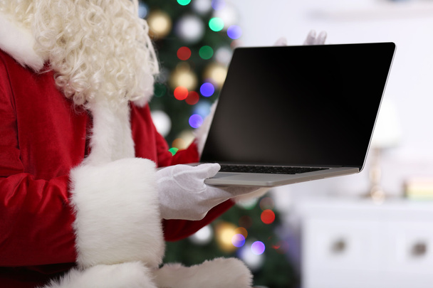 Santa holding laptop on Christmas tree background - Valokuva, kuva