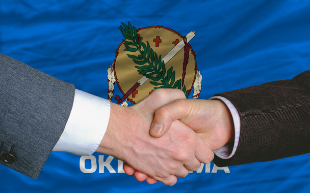 Frente a la bandera del estado americano de Oklahoma dos hombres de negocios mano
 - Foto, Imagen
