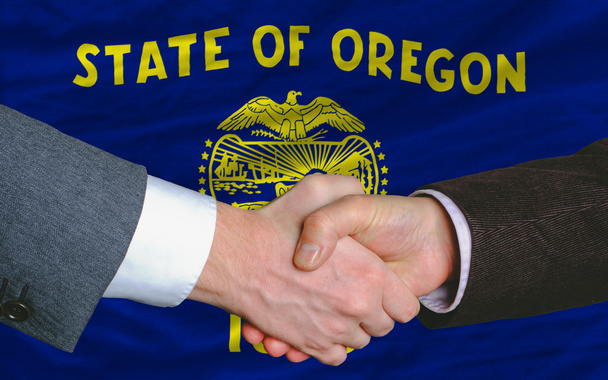Frente a la bandera del estado americano de Oregon dos hombres de negocios handsh
 - Foto, imagen