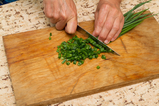 Szakács aprítás egy zöld hagyma, egy késsel, a vágódeszka - Fotó, kép