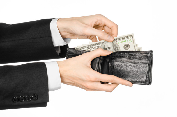 Money and business topic: hand in a black suit holding a wallet with dollar banknotes isolated on white background in studioMoney and business topic: hand in a black suit holding a wallet with dollar - Valokuva, kuva