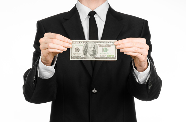 Money and business theme: a man in a black suit holding a bill of 100 dollars and features a hand gesture on an isolated white background in studio - Foto, immagini