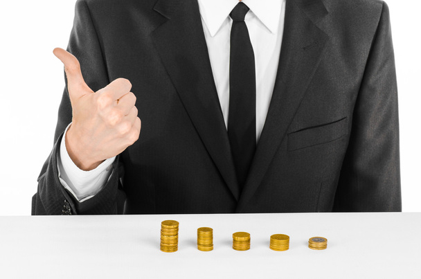 Money and business theme: a man in a black suit indicates the chart bars of gold coins on a white table in the studio on a white background isolated - Foto, afbeelding