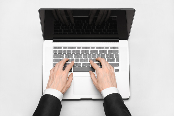 Business and technology topic: the hand of man in a black suit showing gesture against a gray and white background laptop in the studio isolated top view - Foto, imagen
