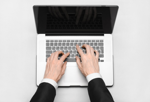 Business and technology topic: the hand of man in a black suit showing gesture against a gray and white background laptop in the studio isolated top view - Zdjęcie, obraz
