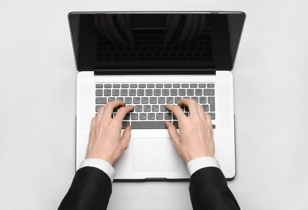 Business and technology topic: the hand of man in a black suit showing gesture against a gray and white background laptop in the studio isolated top view - Zdjęcie, obraz