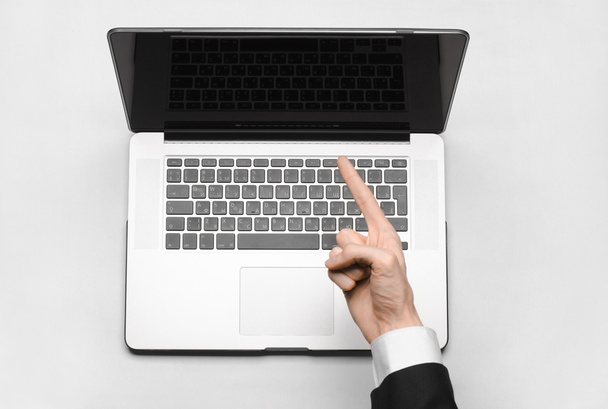 Business and technology topic: the hand of man in a black suit showing gesture against a gray and white background laptop in the studio isolated top view - Photo, Image