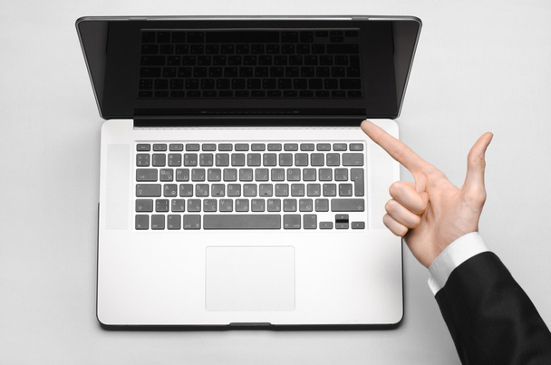 Business and technology topic: the hand of man in a black suit showing gesture against a gray and white background laptop in the studio isolated top view - Foto, Imagen