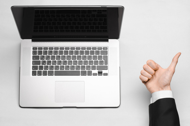 Business and technology topic: the hand of man in a black suit showing gesture against a gray and white background laptop in the studio isolated top view - Photo, Image