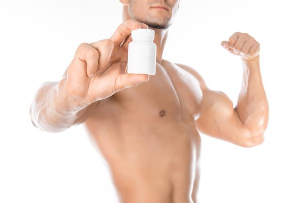Bodybuilding and chemical additives: handsome strong bodybuilder holding a white jar of pills on white isolated background in studio - Foto, Imagem