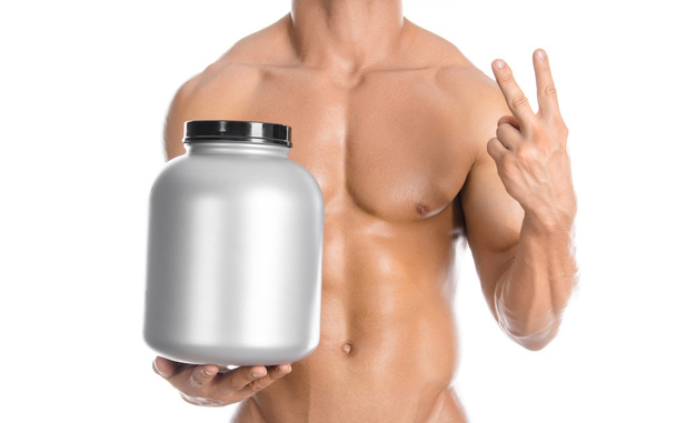Bodybuilding and Sports theme: handsome strong bodybuilder holding a plastic jar with a dry protein and showing gesture isolated on white background in studio - Foto, imagen