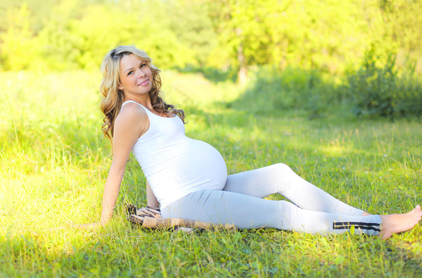 Heureuse femme enceinte souriante à l'extérieur sur l'herbe en été ensoleillé d
 - Photo, image