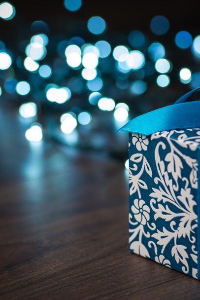 Подарочная коробка с голубым луком и огнями на деревянной поверхности
 - Фото, изображение