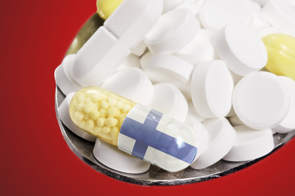 Colher cheia de comprimidos e uma cápsula com a bandeira da Finlândia
 - Foto, Imagem