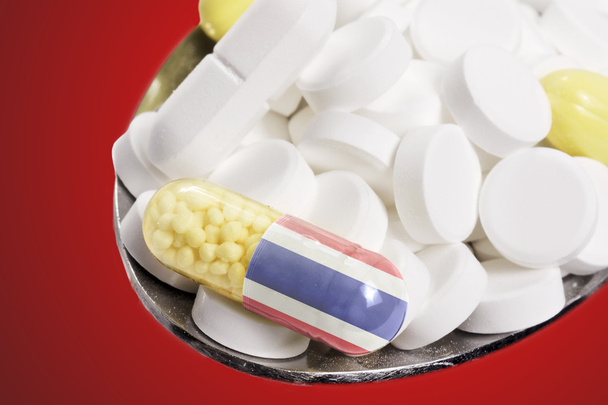 Cuchara llena de pastillas y una cápsula con el diseño de la bandera de Tailandia
 - Foto, Imagen